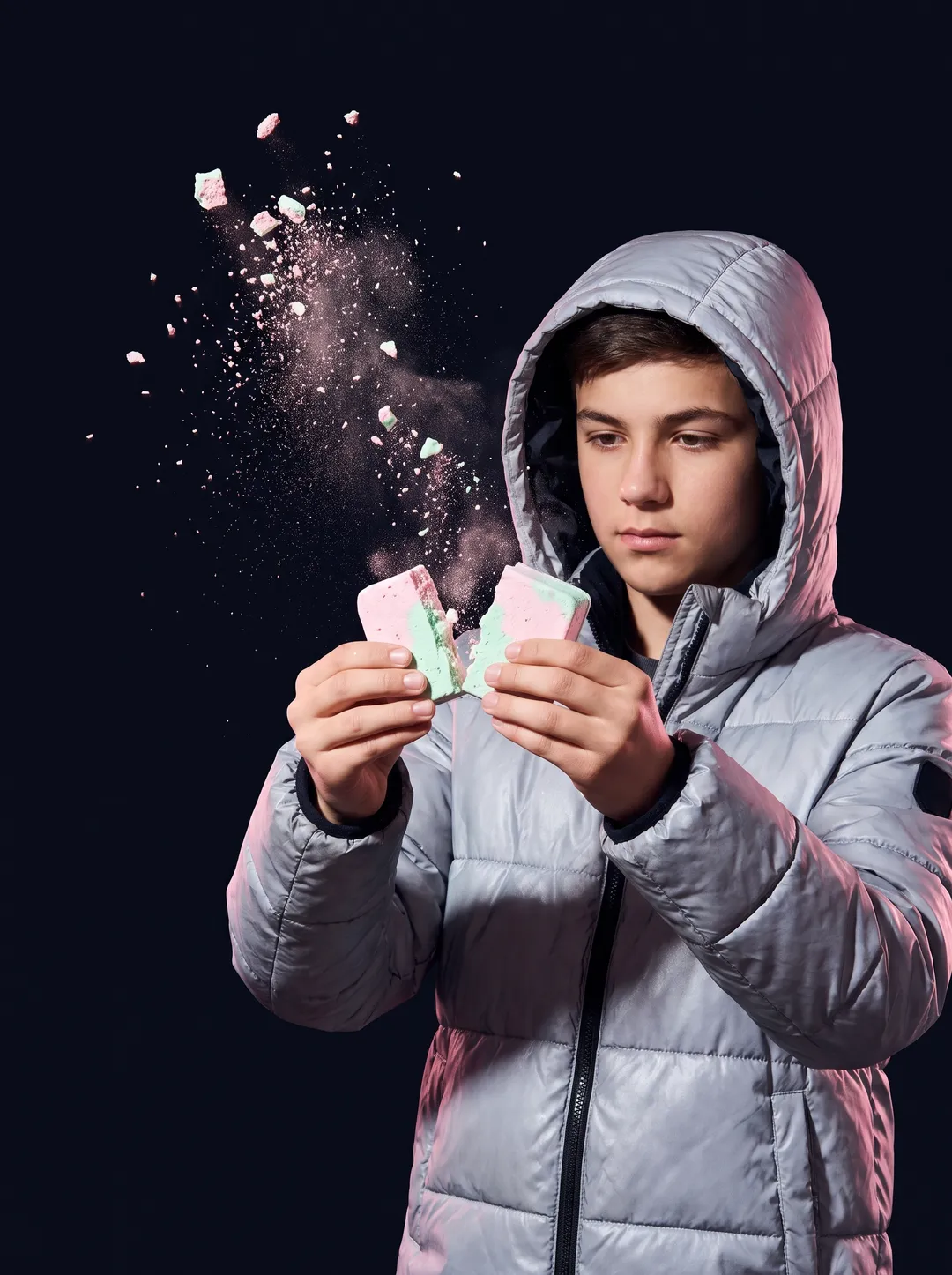 A teenager in a silver puffer jacket snapping a pastel freeze-dried ice cream bar against a solid midnight backdrop